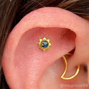 Flat piercing featuring an anodized sun cabochon with a black opal